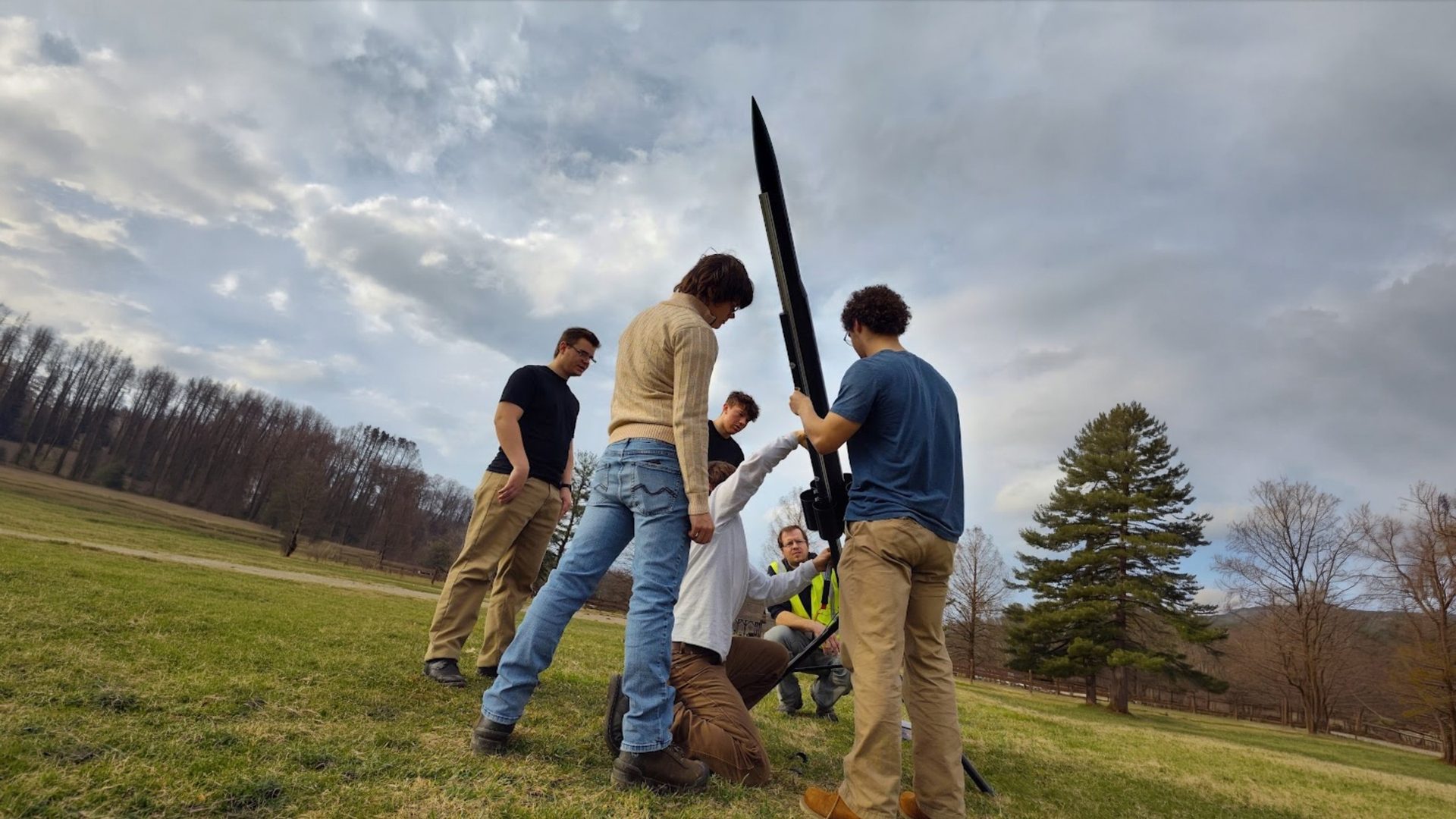 Club members loading a rocket onto a yellow launch rail at a grassy field
