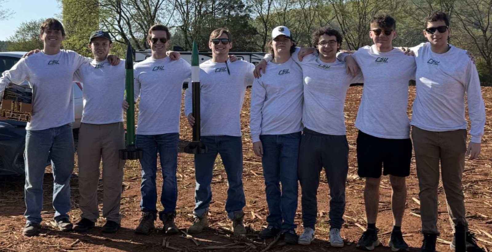 Club members around a white rocket on a launch field